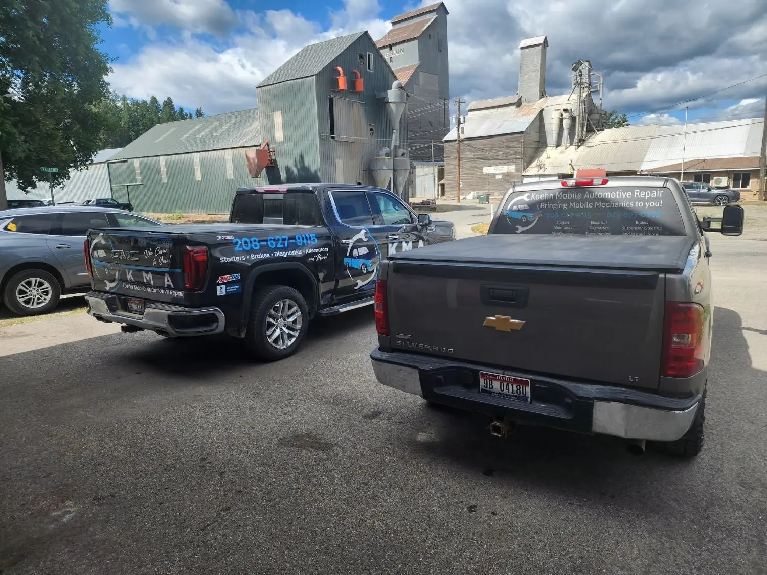 Two Koehn Mobile Automotive service trucks, a black GMC with KMA graphics and a gray Chevrolet Silverado with lettering on the back window